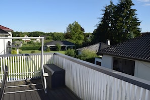 Ein Wohnbalkon mit weißer Brüstung, einem Grill und Blick auf Nachbarhäuser und Bäume.