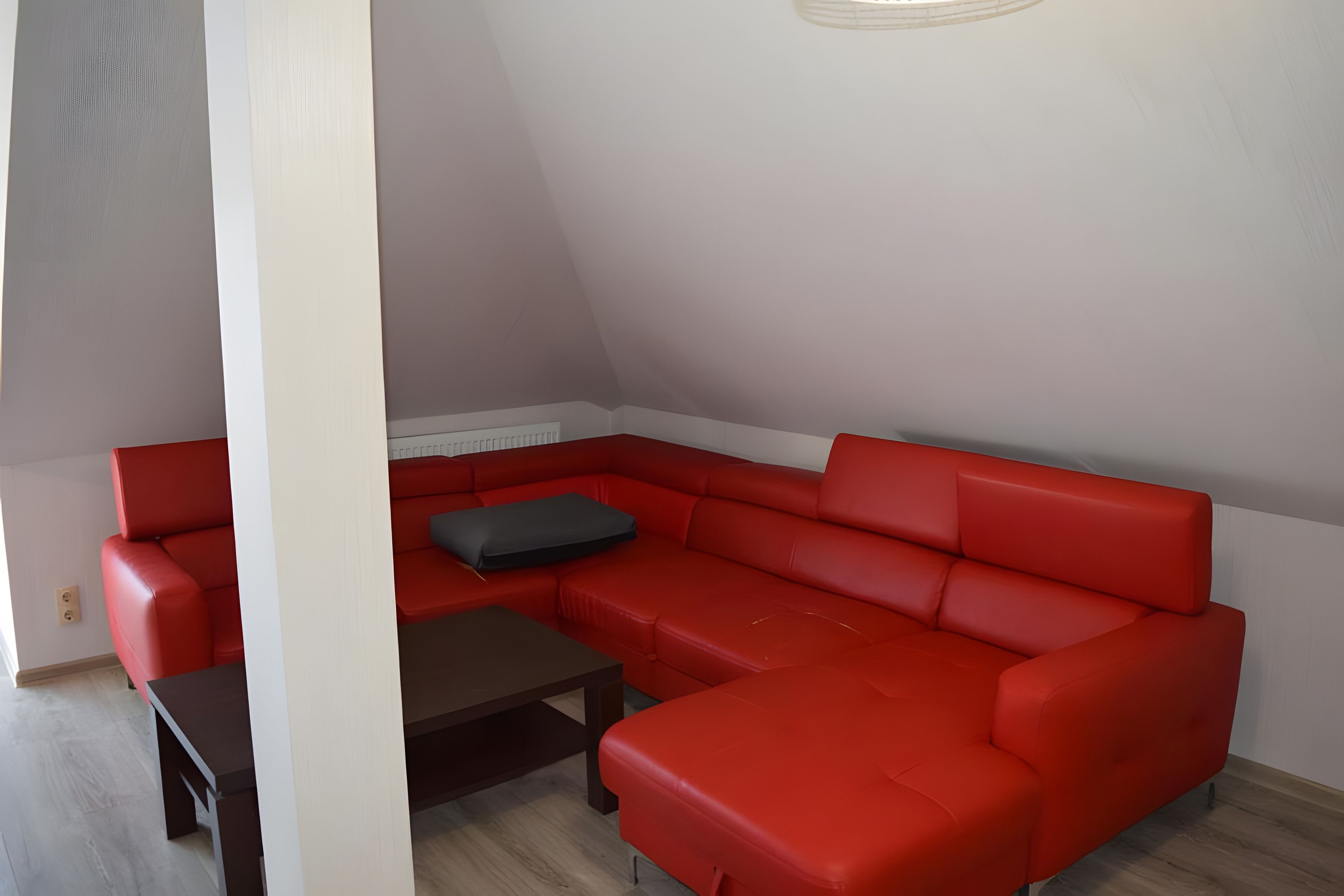 Ein rotes Ecksofa mit einem dunkelbraunen Couchtisch in einem Raum mit weißen Wänden und einer geneigten Decke.