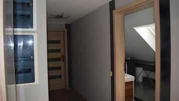 Un pasillo estrecho con una puerta de madera, un muro de cristal con persianas y un ventilador de techo.