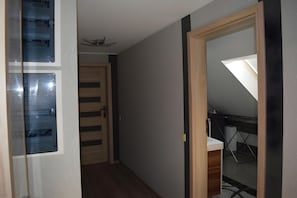 Ein schmaler Flur mit einer Holztür, einer Glaswand mit Jalousien und einem Deckenventilator.