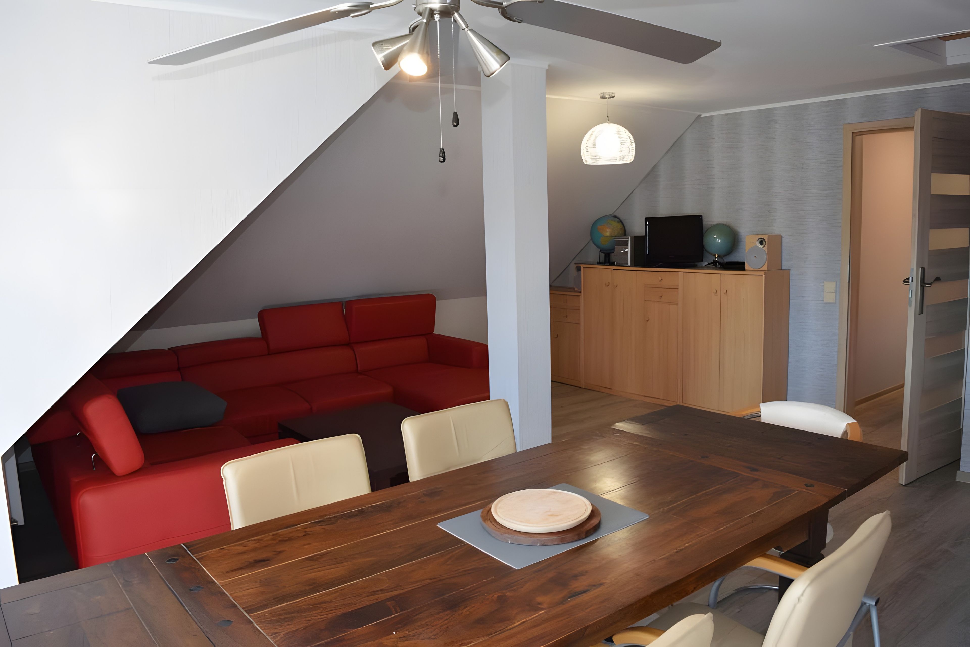A dining area with a wooden table, a red sofa, and a ceiling fan.
