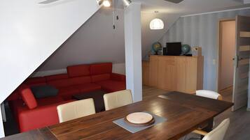 A dining area with a wooden table, a red sofa, and a ceiling fan.