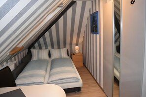 A bedroom with a sloped ceiling, a bed with striped bedding, a bedside table with a lamp, and a framed picture on the wall.