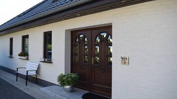 A building with a white brick exterior, a dark brown door with glass panels, a bench, and potted plants.