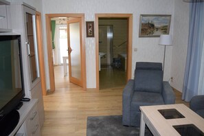 Een woonkamer met een televisie, een grijze bank en een eettafel.