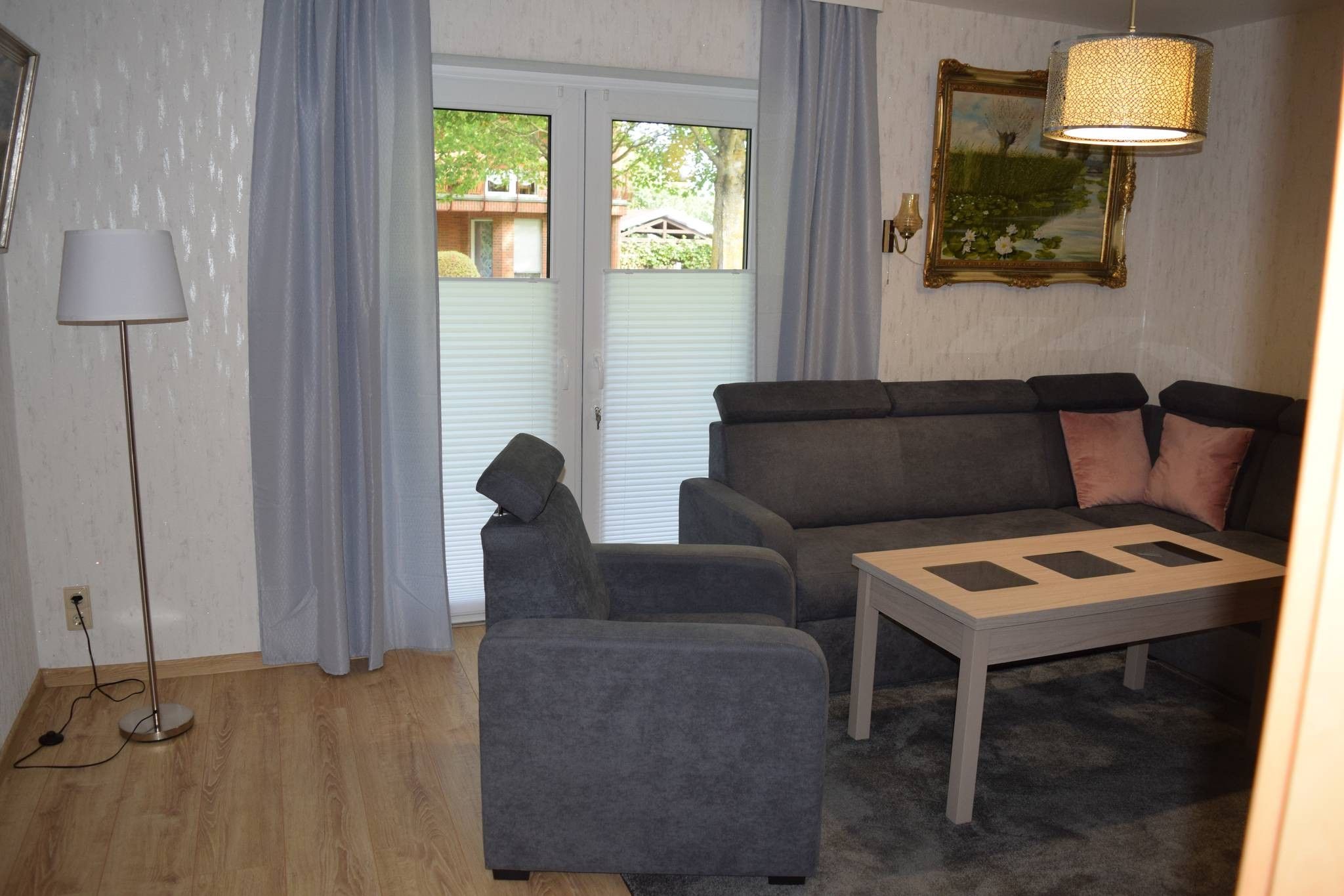 Ein Wohnzimmer mit einer Couch, einem Sessel und einem Couchtisch, einer Stehlampe und einem Bild an der Wand.