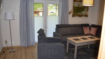 Ein Wohnzimmer mit einer Couch, einem Sessel und einem Couchtisch, einer Stehlampe und einem Bild an der Wand.