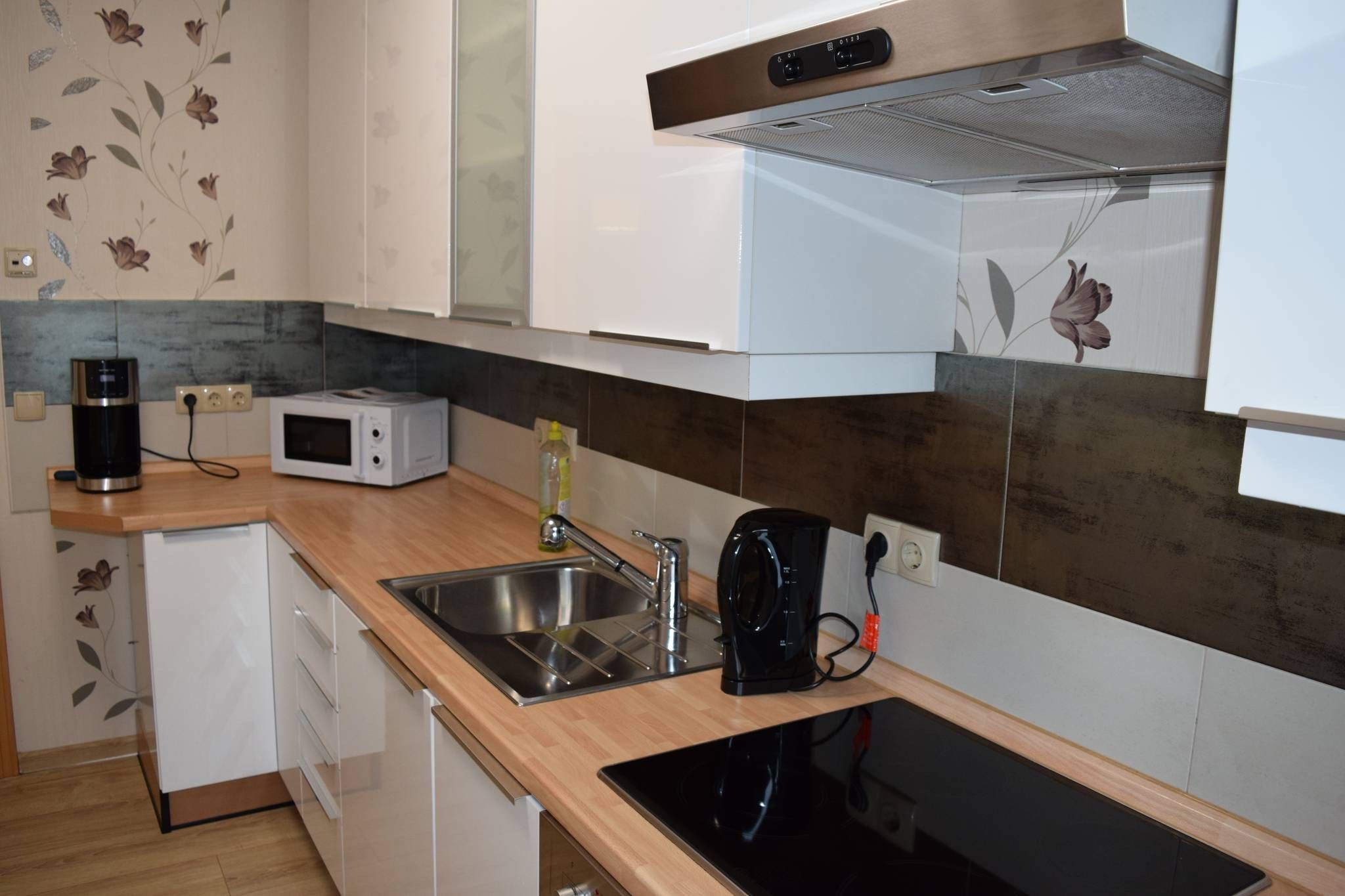 A compact kitchen with a microwave, coffee maker, sink, and a black induction cooktop.