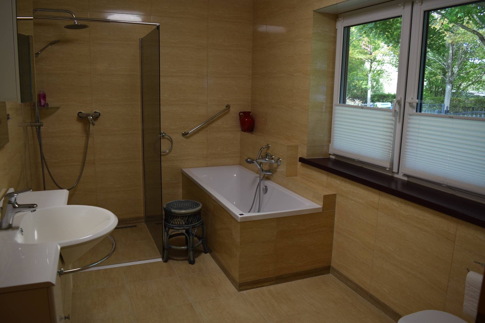 A modern bathroom with a walk-in shower, a freestanding bathtub, a sink, and a window with blinds.