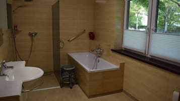 A modern bathroom with a walk-in shower, a freestanding bathtub, a sink, and a window with blinds.