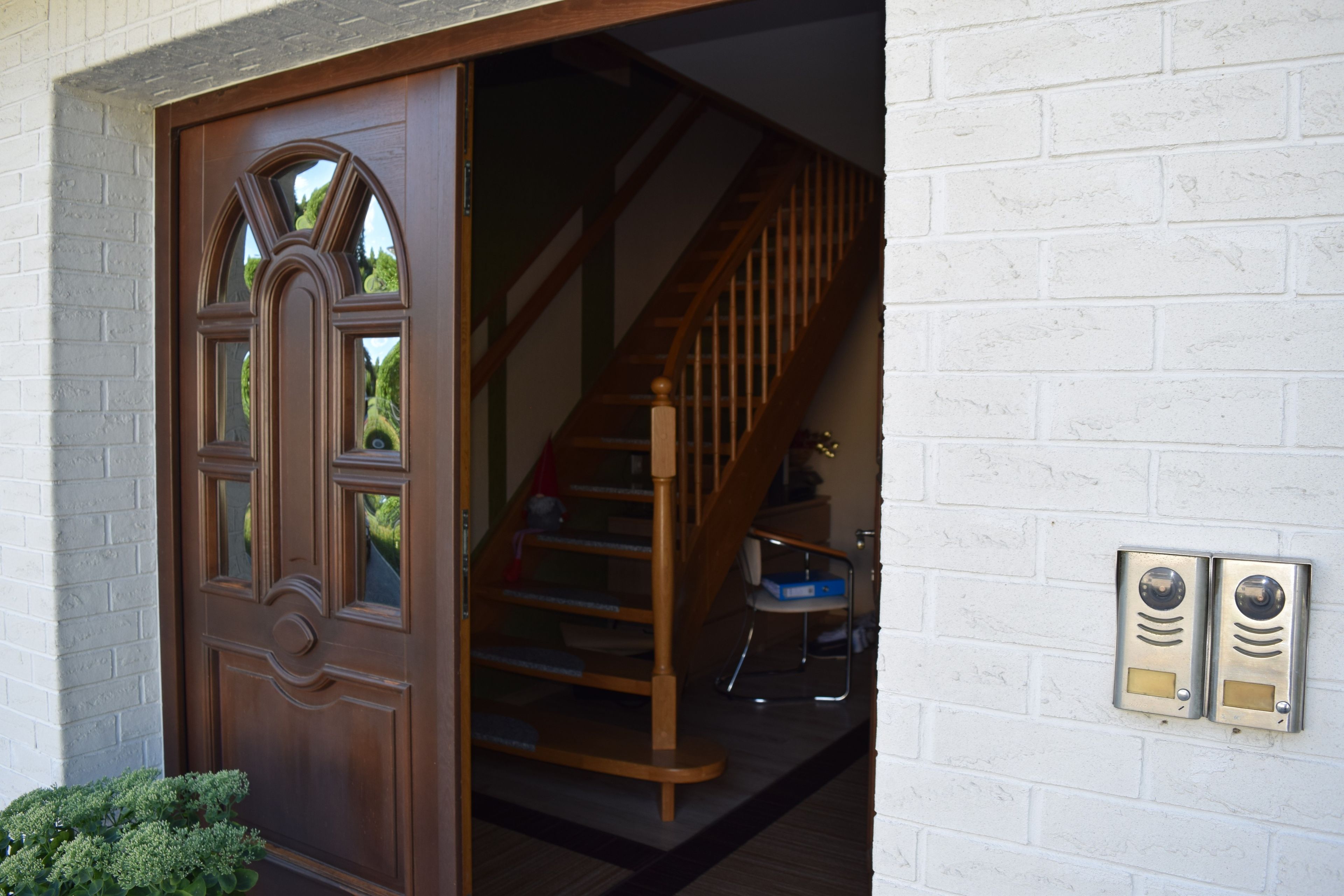 A wooden door with a glass panel, a staircase with wooden railings, and a white brick wall.
