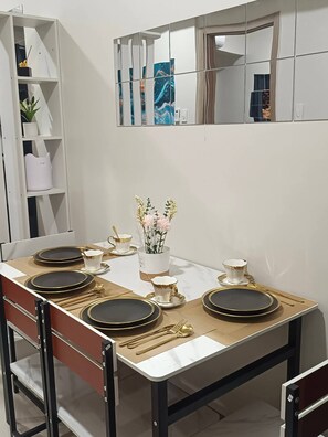 A dining table set with black plates, gold cutlery, and a vase with flowers. - Modern, Comfortable Apartment in Central Pasay, Philippines (Pasay)