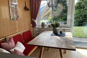 A wooden table with a bench, a window with a view of greenery, and a wall-mounted poster. - Alpenflair holiday apartment 309 (Oberstdorf)