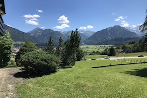 A mountainous landscape with a clear sky, a grassy area with trees, and a distant village. - Alpenflair holiday apartment 309 (Oberstdorf)
