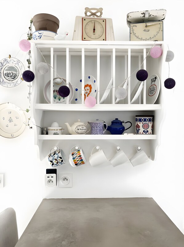 Una estantería blanca con diversos utensilios de cocina, como una tetera, platos y tazas.