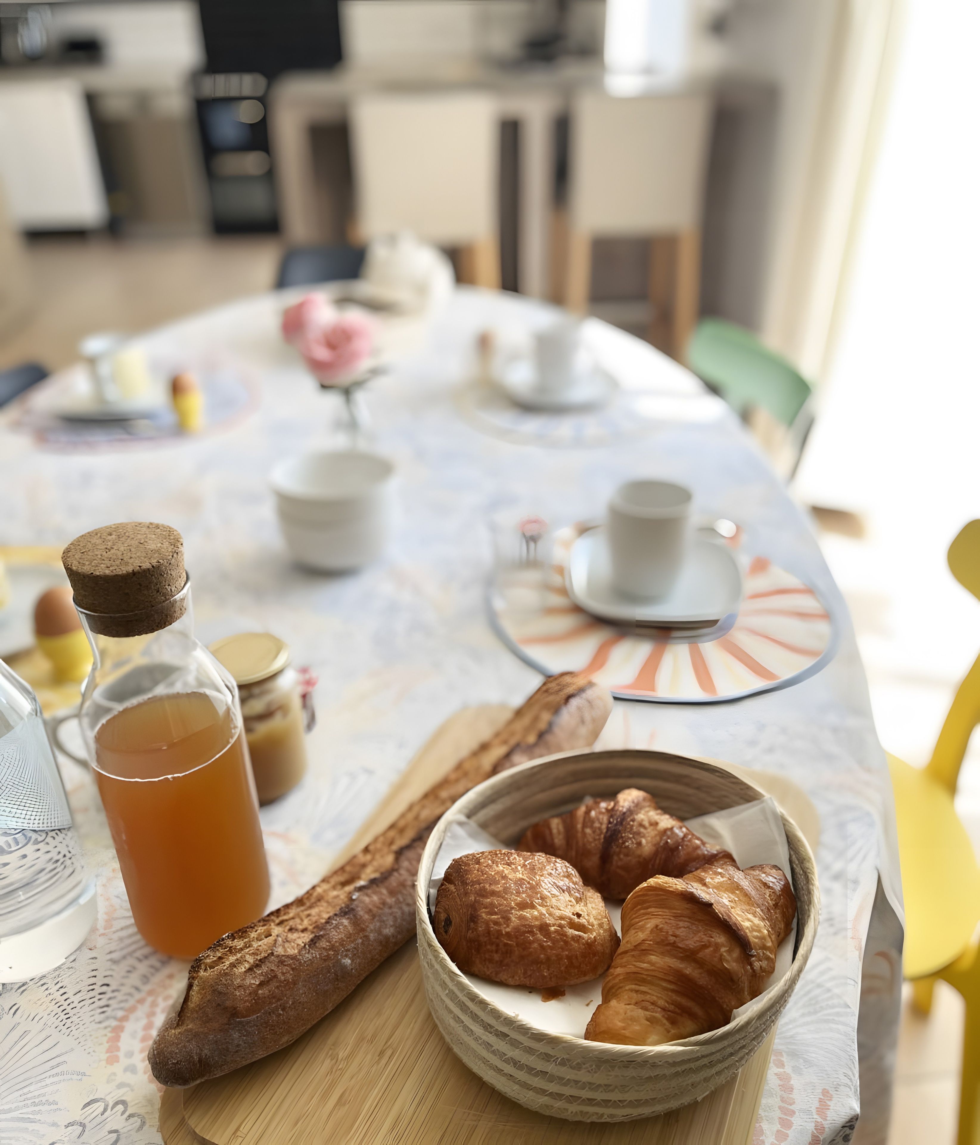 A breakfast setting with croissants, a bottle of juice, and a teapot on a table.