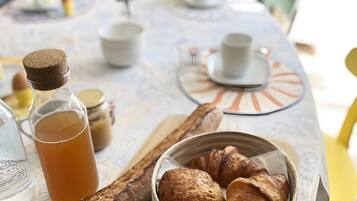 A breakfast setting with croissants, a bottle of juice, and a teapot on a table.