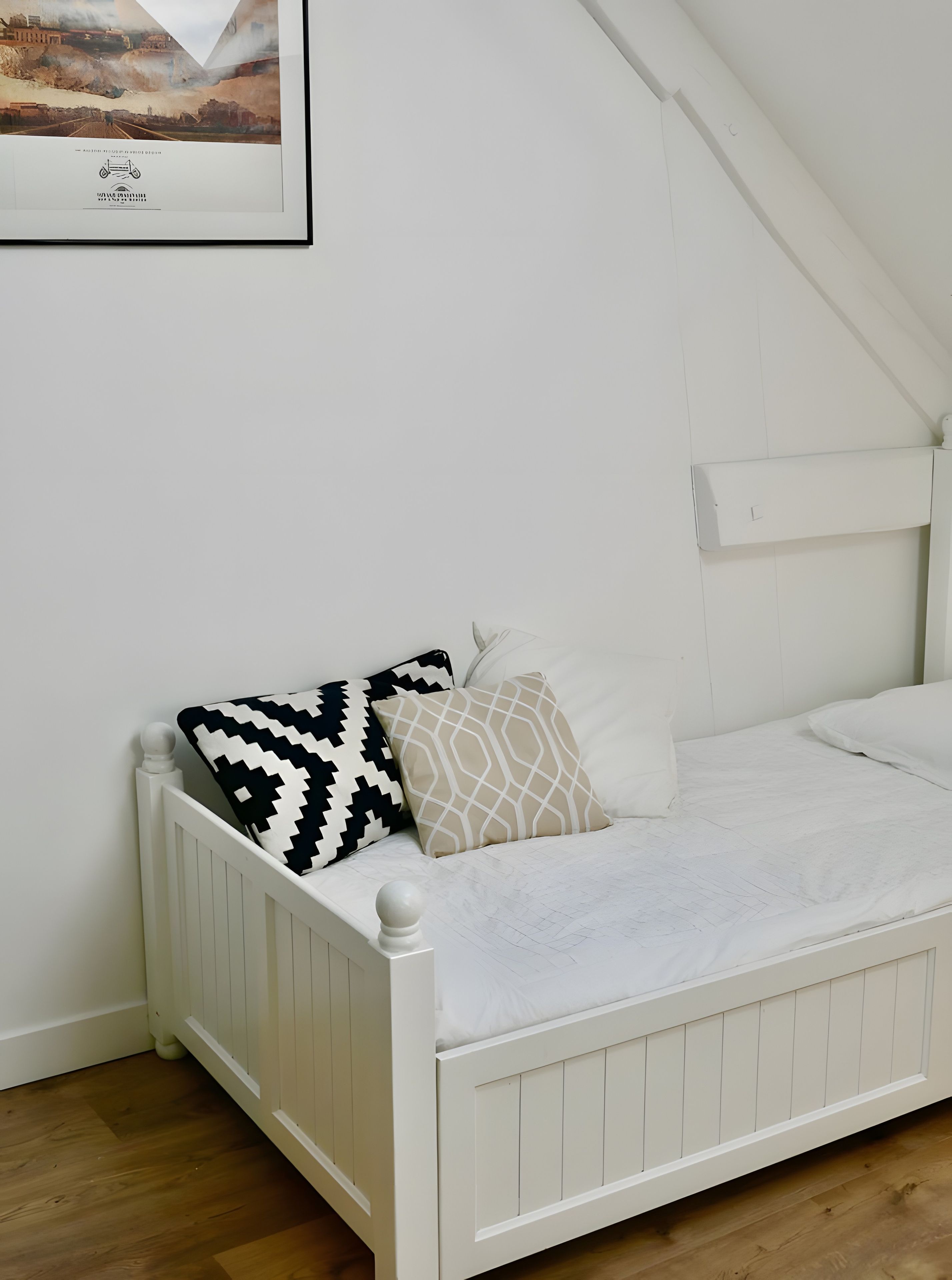 A white bed with patterned pillows, a white headboard, and a framed picture on the wall.