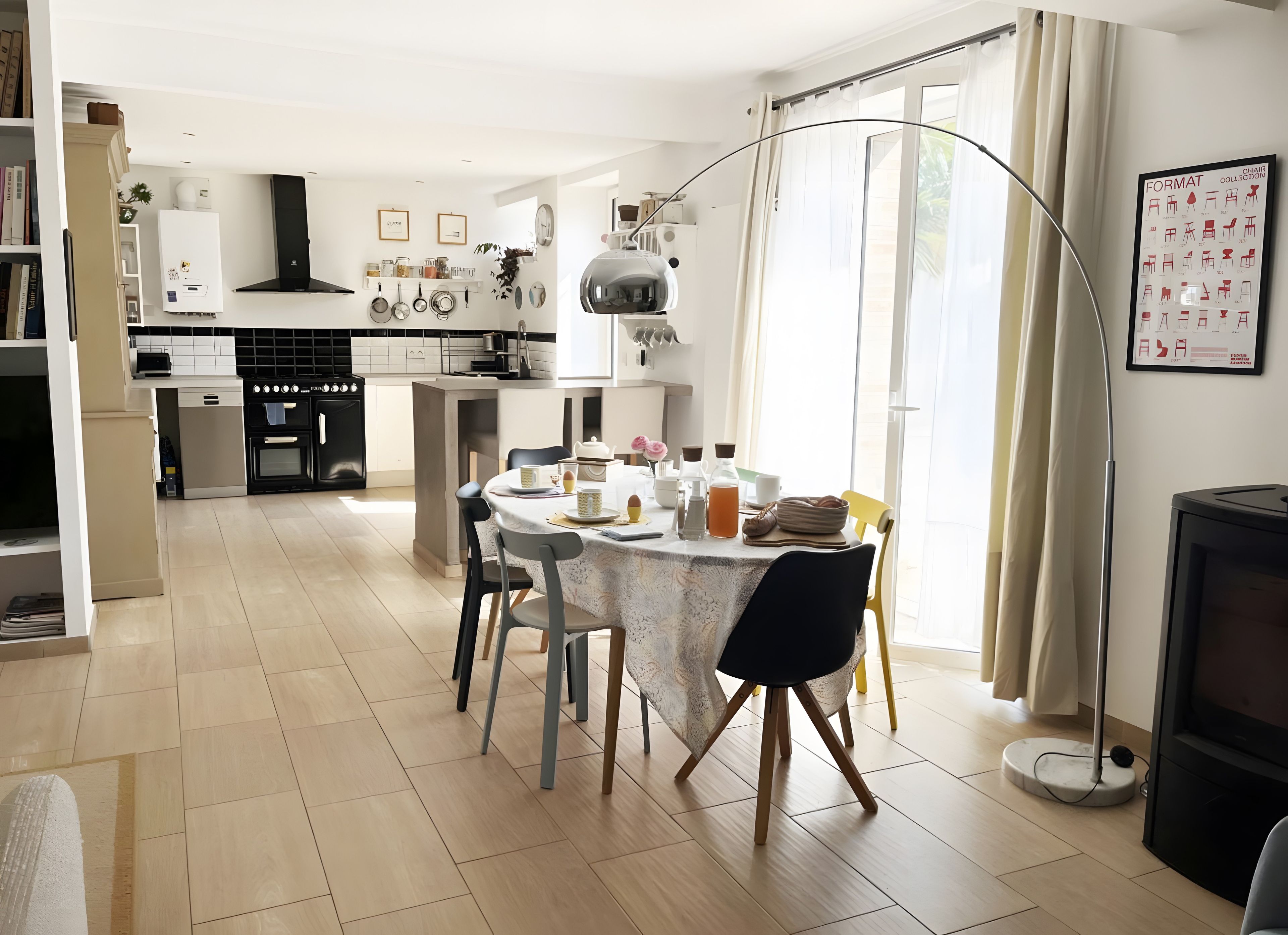 Une cuisine moderne avec des meubles blancs, un coin repas doté d’une table ronde et une grande fenêtre agrémentée de rideaux.