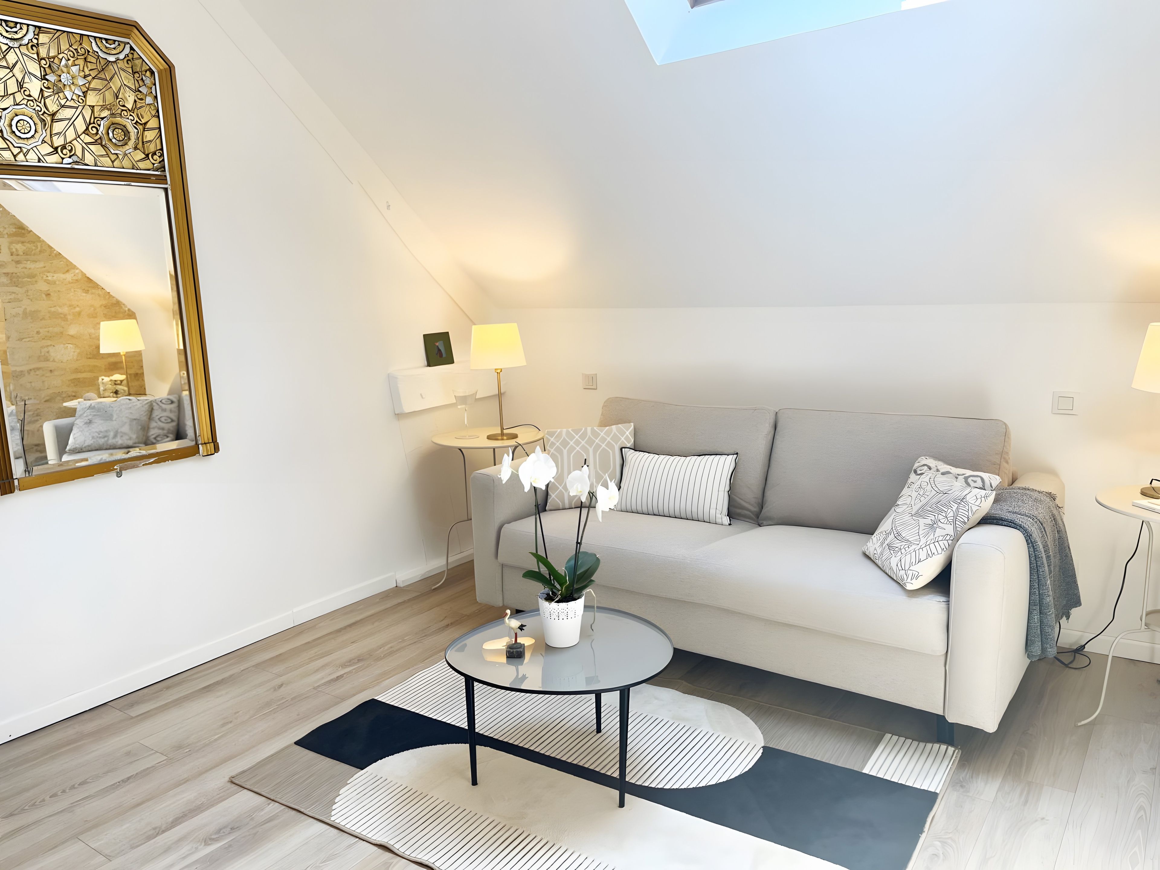 A modern living room with a sofa, coffee table, lamps, and a decorative mirror.