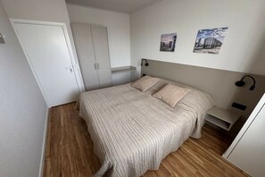 A bedroom with a bed, wooden flooring, a wardrobe, and two wall-mounted pictures. - Holiday apartment with 1 bedroom (Katwijk aan Zee)