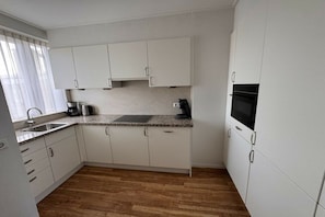 A modern kitchen with white cabinets, a granite countertop, and a built-in microwave. - Holiday apartment with 1 bedroom (Katwijk aan Zee)