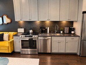 A modern kitchen with grey cabinets, stainless steel appliances, and a yellow sofa. - Stylish Downtown 1BR | Walkable to NFL (Pittsburgh)