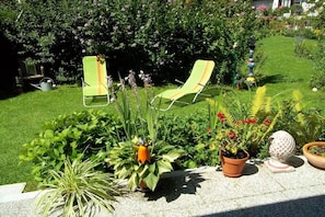 Ein Garten mit zwei Liegestühlen, verschiedenen Topfpflanzen und einer Zierkugel.
