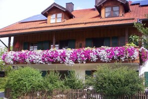 Puinen rakennus, jossa on parveke, joka on koristeltu kukilla, puinen aita ja aurinkopaneelit katolla.