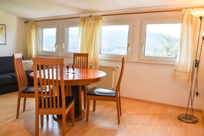 A dining area with a round table and chairs, large windows with curtains, a radiator, and a floor lamp. - Holiday apartment with 1 bedroom (Titisee-Neustadt)