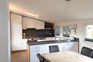 A modern kitchen with white cabinets, a wooden countertop, and a dining area with a table and chairs. - Holiday apartment with 1 bedroom (Titisee-Neustadt)