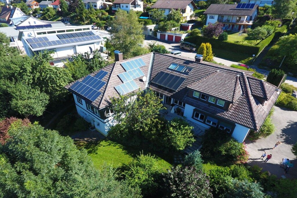 A residential area with houses, some with solar panels, surrounded by greenery.