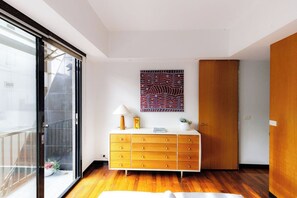 Ein modernes Zimmer mit Holzboden, einer weißen Kommode mit Schubladen, einem Wandbild und einer Schiebeglastür.