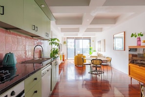 A modern kitchen with a dining area, featuring a large window, a plant, and a wooden dining table. - Stylish 3BDR Retreat in the Heart of Melbourne (Melbourne)