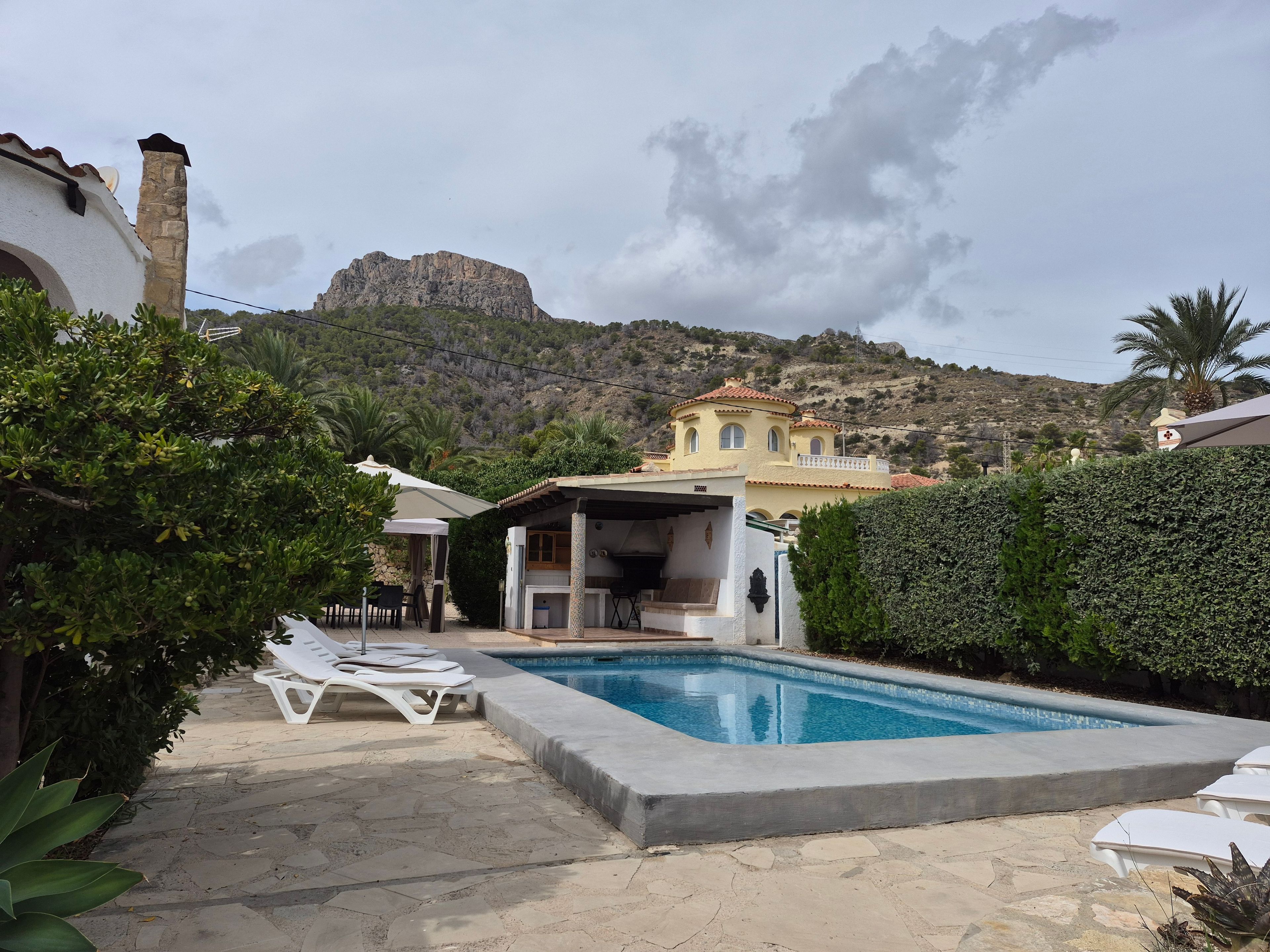 Zona de piscina con sillones, un área de estar techada y vistas a la montaña.