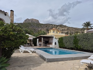 Zona de piscina con sillones, un área de estar techada y vistas a la montaña.