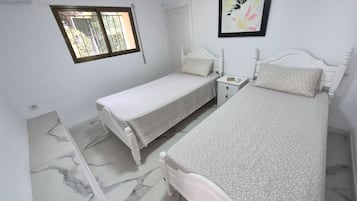 A bedroom with two single beds, a bedside table with a lamp, a window, and a framed picture on the wall.