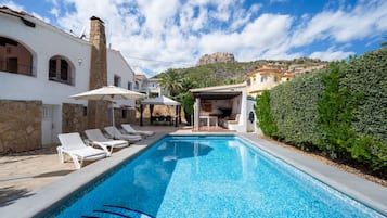 Ein Schwimmbecken mit Liegestühlen, ein Steinhaus und ein Berg im Hintergrund.
