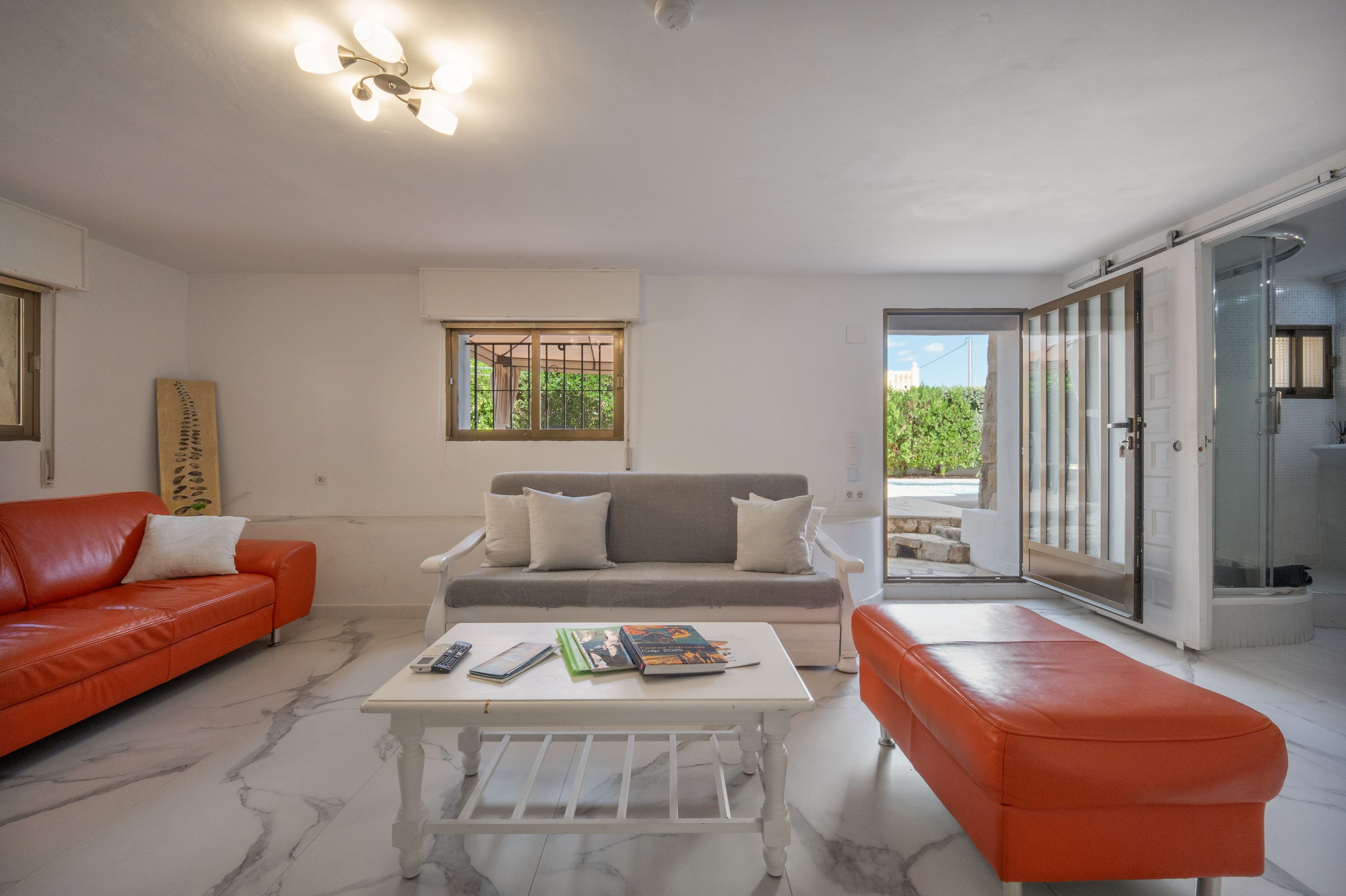 A modern living room with a red sofa, a grey sofa, a white coffee table, and a glass door leading to an outdoor area.
