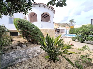 A white building with a stone base, a pool, and a well-maintained garden with various plants and a stone pathway. - Apartment 'Inferior' with Balcony, Wi-Fi and Air Conditioning (Calpe)