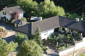 Um imóvel residencial com uma casa grande e um prédio menor anexo, cercado por um jardim com diversas plantas e um caminho de acesso pavimentado.