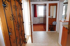 A hallway with a wooden door with metalwork, a radiator, a mirror, and a fan. - Holiday apartment with 1 bedroom (Fischen)