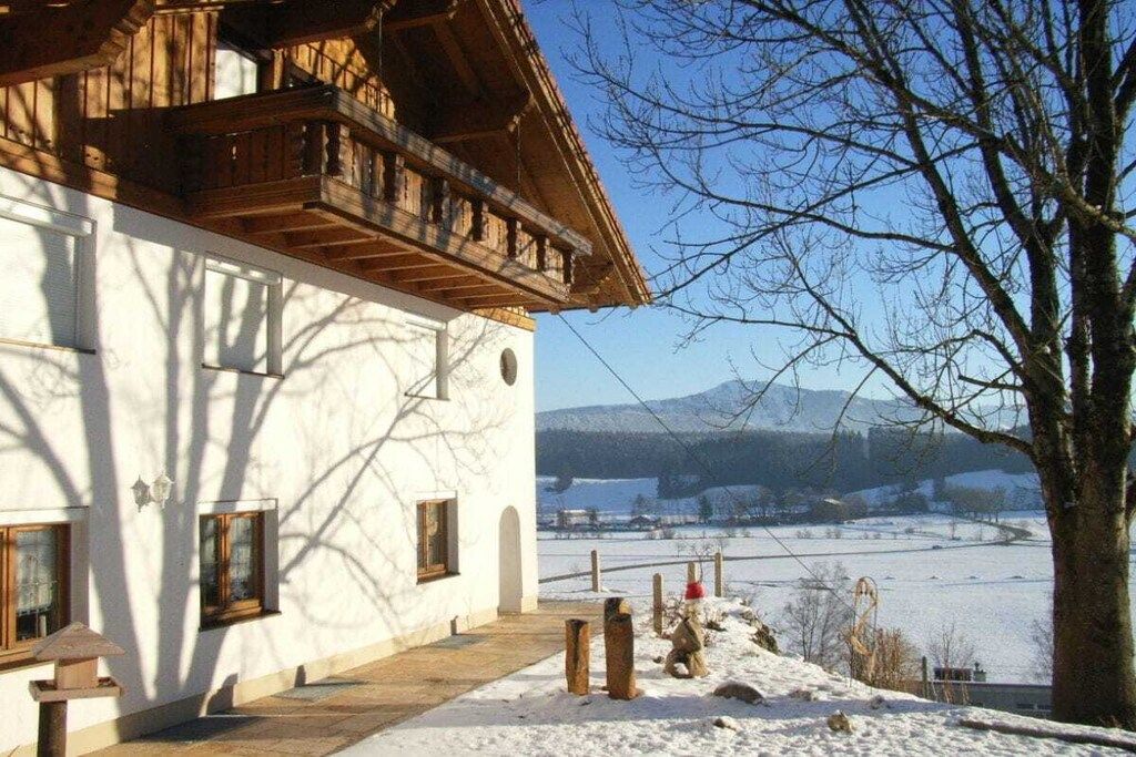 A traditional wooden building with a balcony, a snow-covered landscape, and a clear sky.