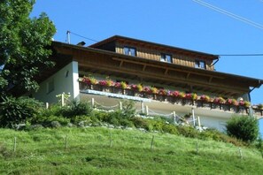 A two-story building with balconies adorned with flowers, surrounded by greenery. - "Grünten" in the Seeblick house (Niedersonthofen)
