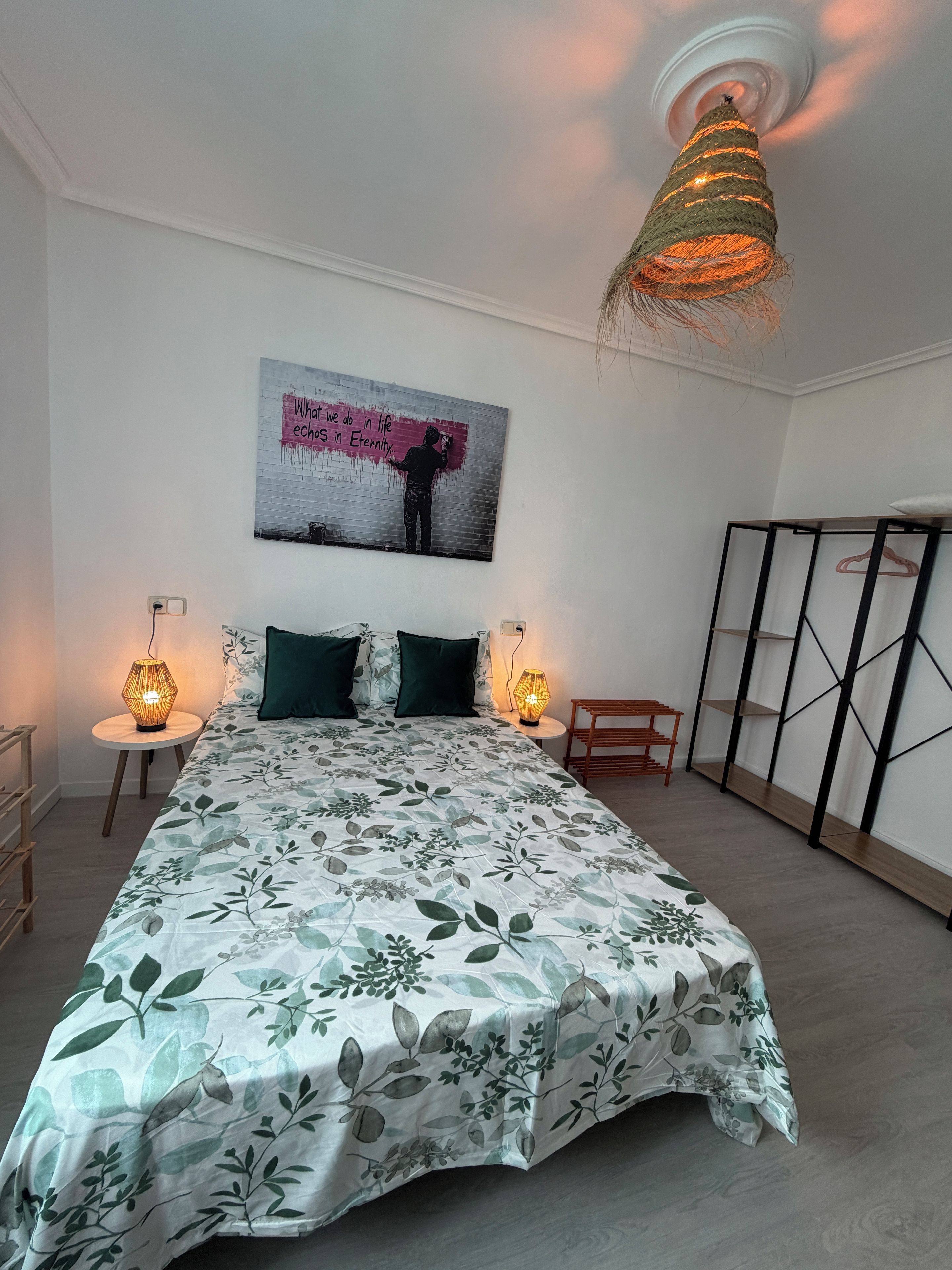Un dormitorio con una cama, dos lámparas de noche, una obra de arte en la pared y una lámpara del techo.