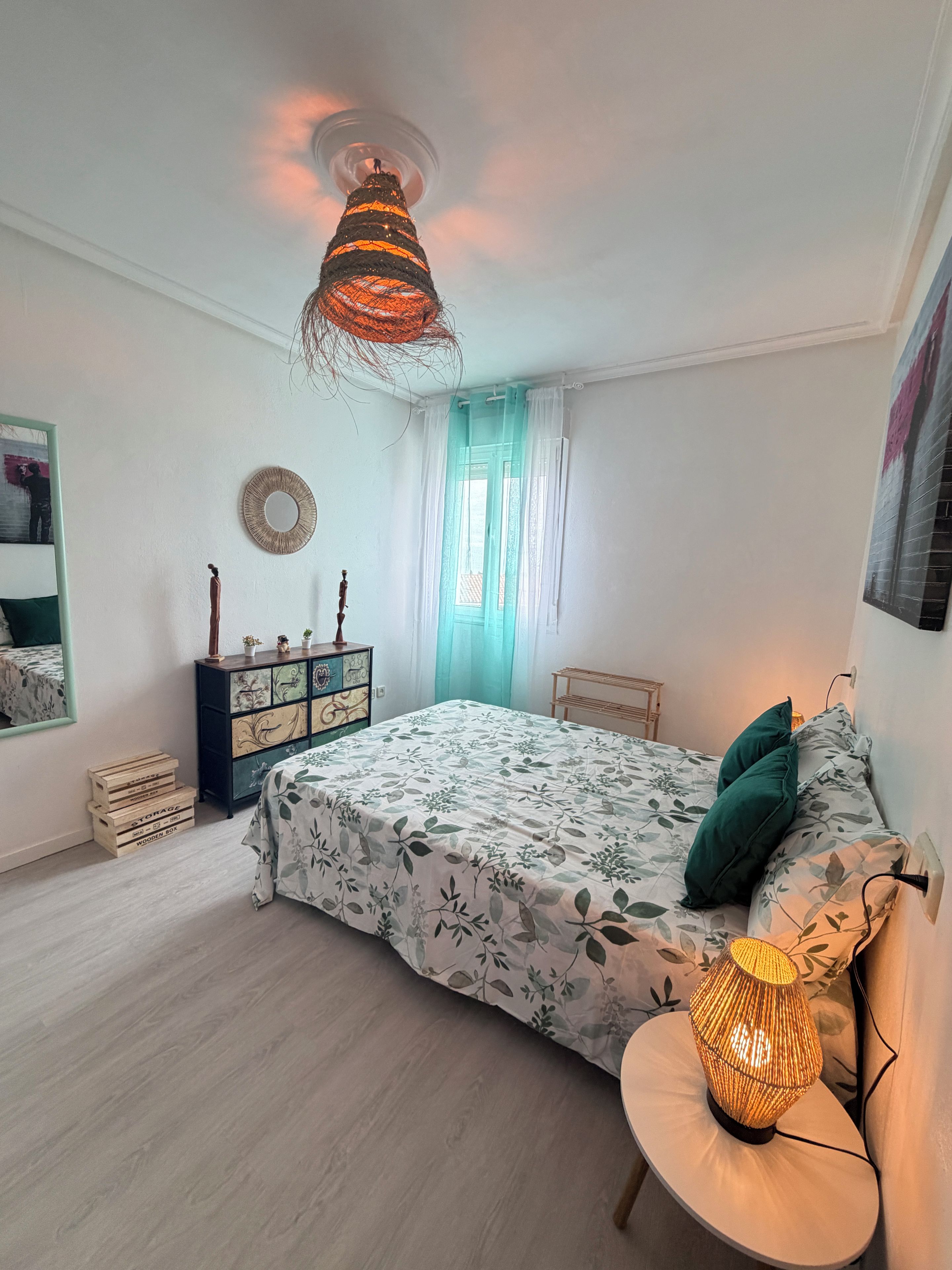A bedroom with a bed, bedside lamp, dresser, and a mirror.
