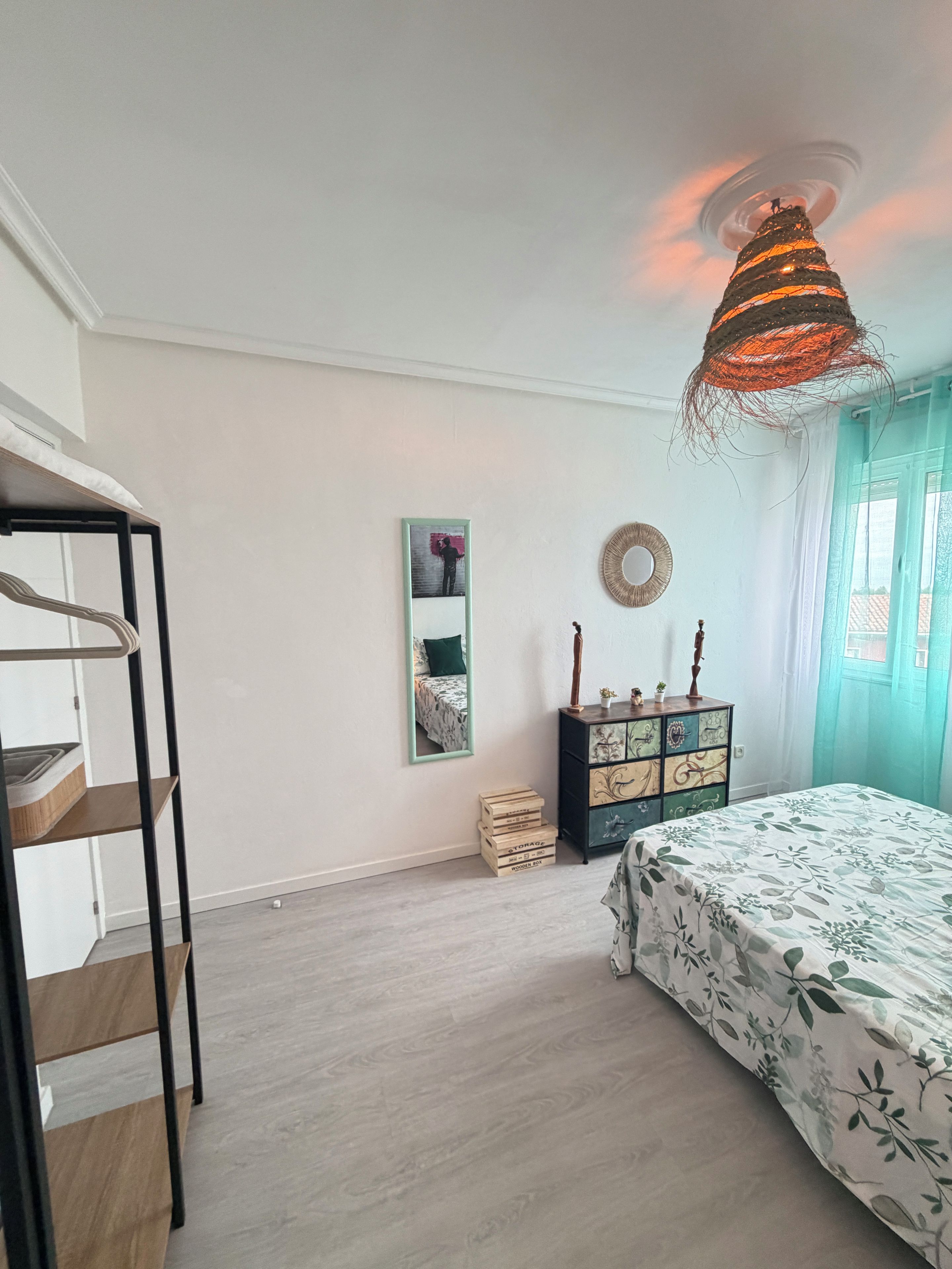 A bedroom with a bed, a dresser, a mirror, and a hanging light fixture.