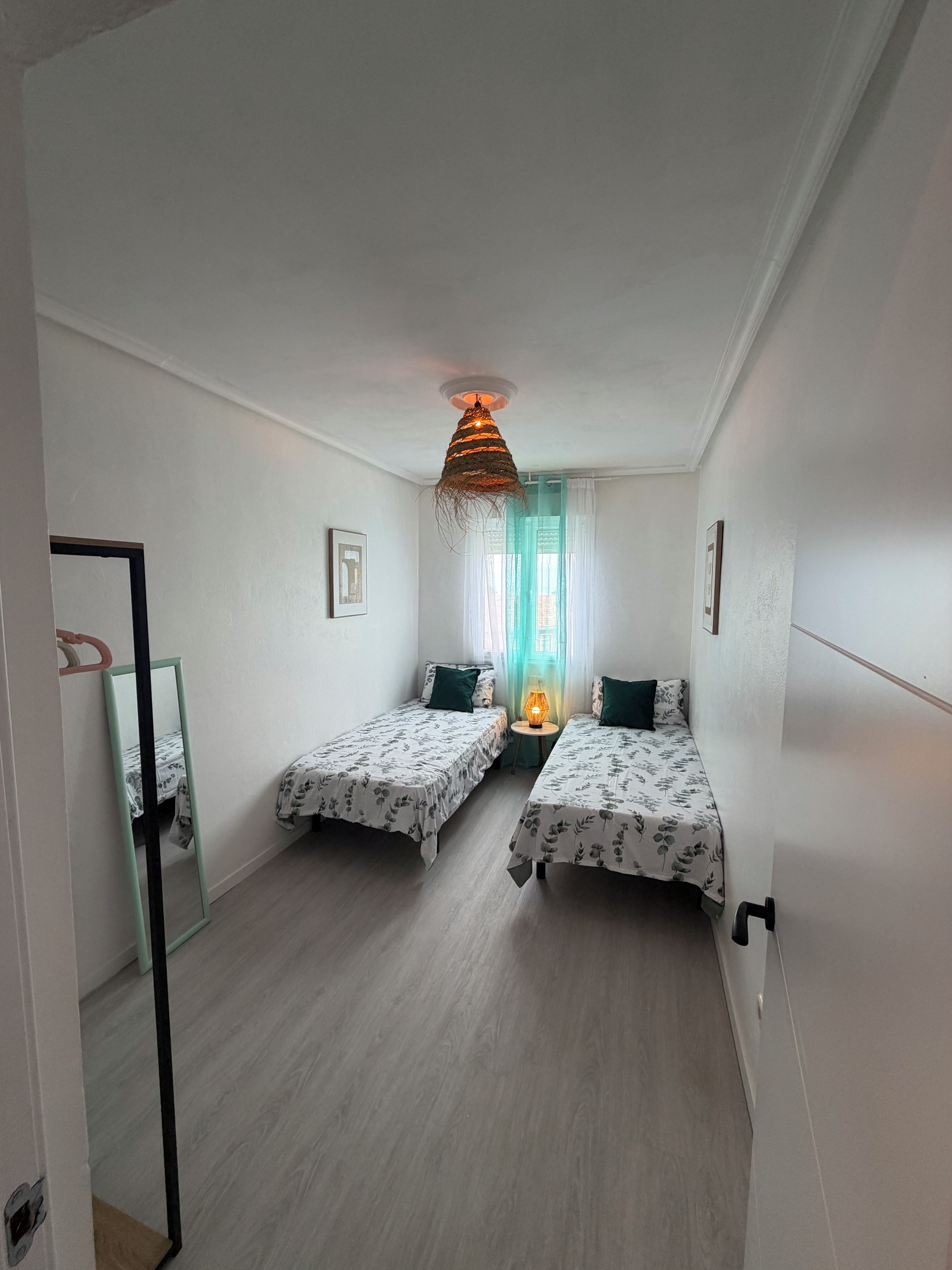 A room with two single beds, a hanging light fixture, and a small table with a lamp.