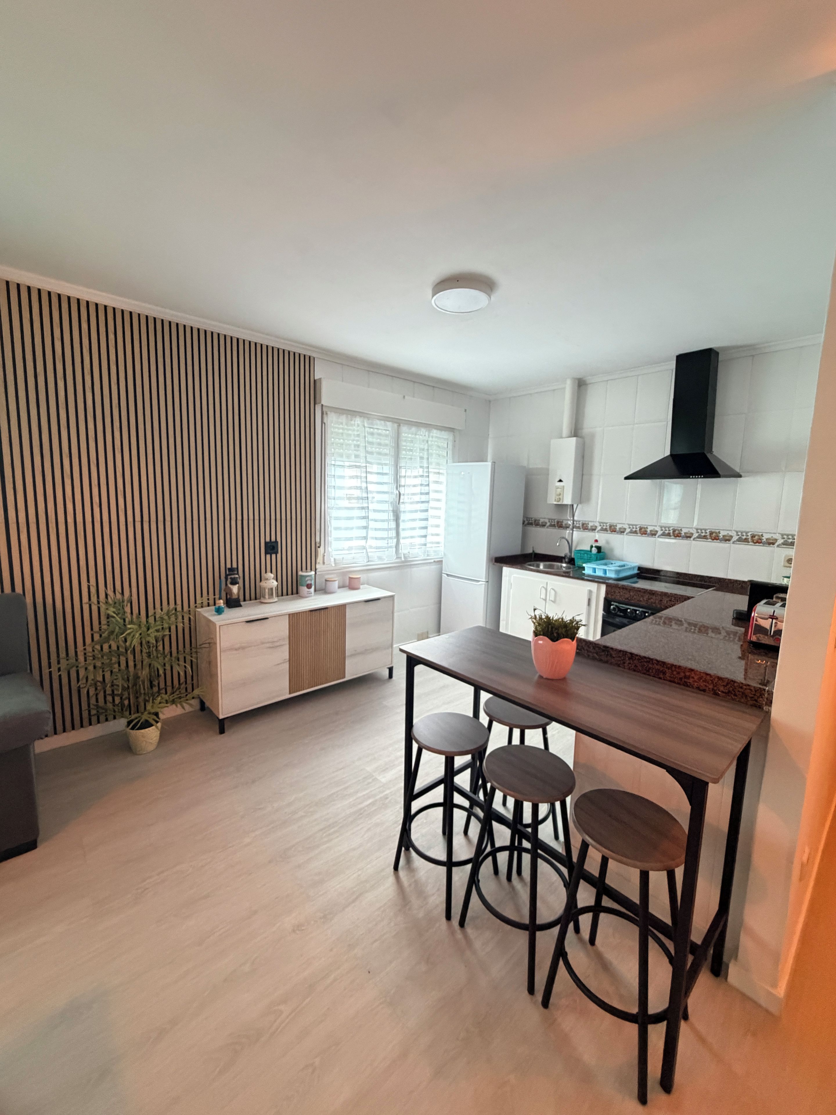 Una cocina moderna con una mesa de comedor de madera y taburetes de bar, horno empotrado y campana extractora negra.