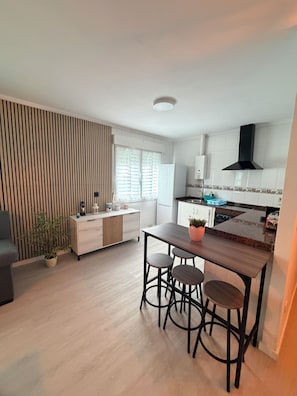 A modern kitchen with a wooden dining table and bar stools, a built-in oven, and a black range hood. - Itos Flats, Cudillero (La Atalaya)